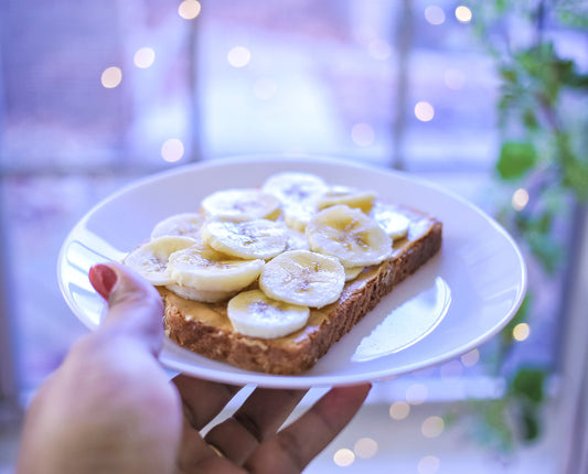 Image of a hand holding a plate with peanut butter banana toast