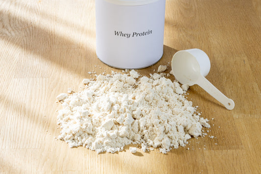 Whey protein powder spilled next to a container and scoop.