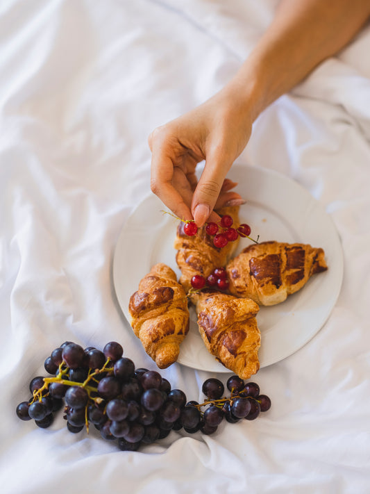 Image of a woman picking at croissants and grapes to convey the need for sleep supplements - WAYT Nutrition